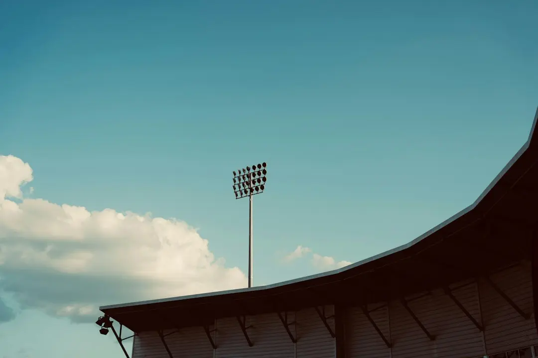 A stadium floodlight tower above the edge of a stand roof against a blue sky, for the six sports Nufu TV streams